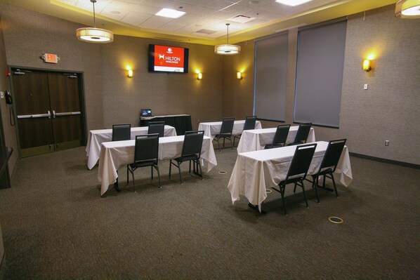 Un salón de conferencias con mesas dispuestas para reuniones, una pantalla de proyector y un televisor mostrando el logotipo de Hilton Worldwide.