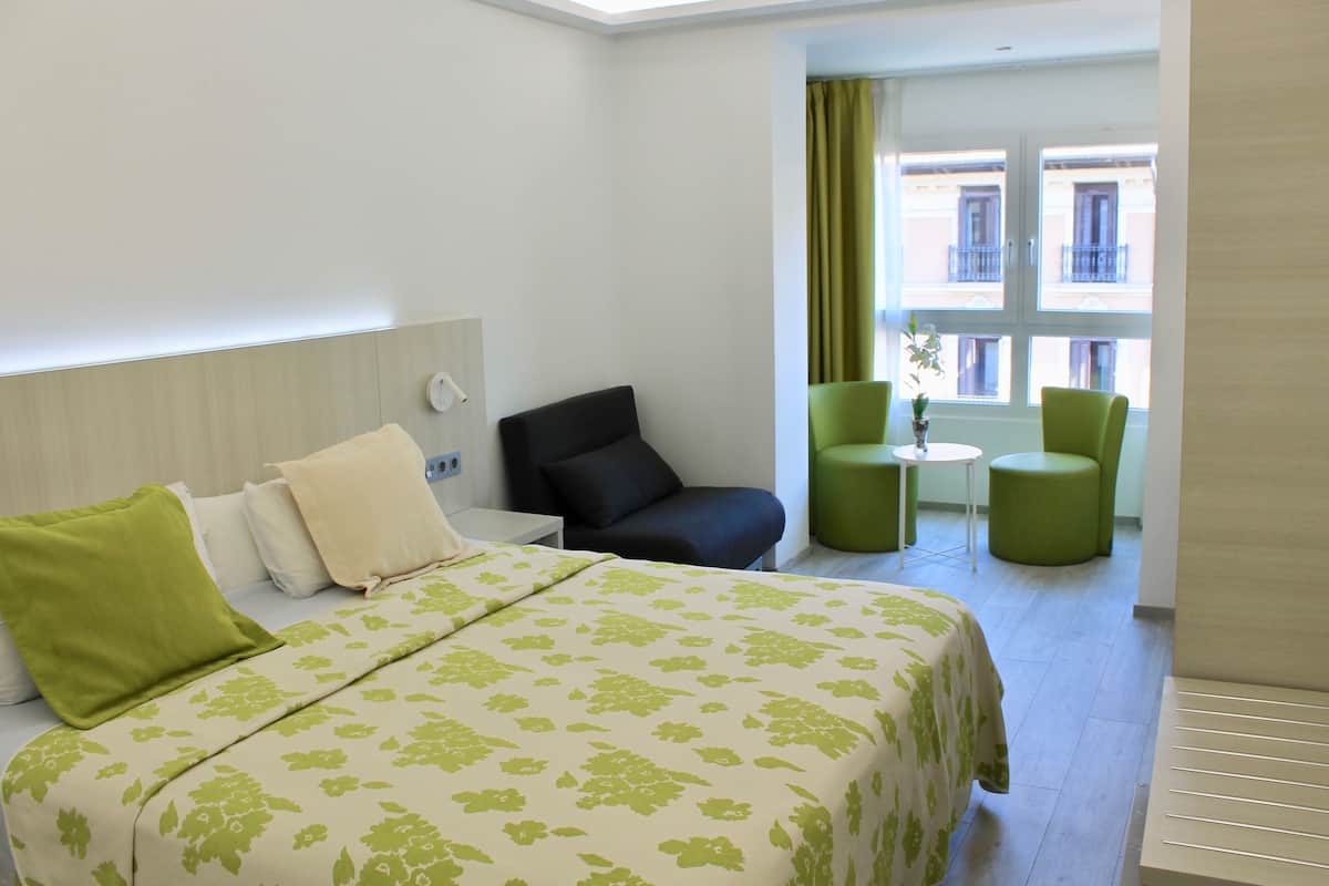Quarto de hotel com cama, escrivaninha, cadeira e vista para o exterior.