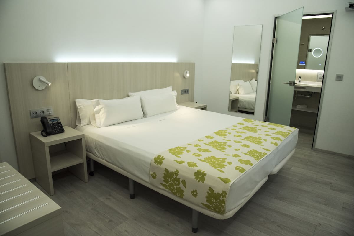 Quarto de hotel com cama, mesa de cabeceira e espelho.
