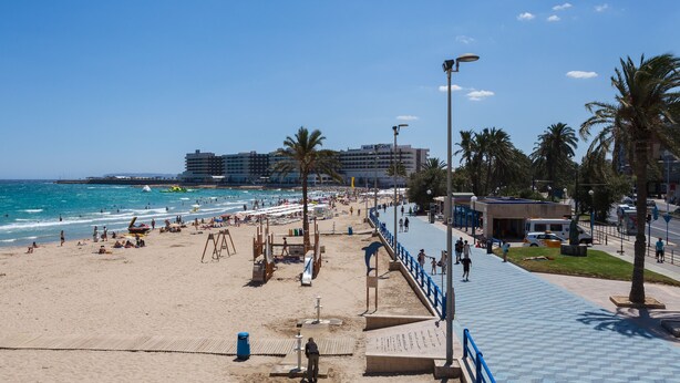 Una playa con un paseo marítimo, palmeras y un hotel llamado "MELIA PICANTE" al fondo.