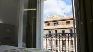 Habitación de hotel con balcón, cama y vista a un edificio con balcones.