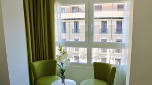 Una habitación con dos sillas verdes, una mesita blanca y un jarrón con flores.