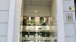 Una entrada a un edificio con puerta de vidrio, un cartel con la letra “H” y un letrero que indica conexión a un sendero para bicicletas.