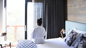 A hotel room with a bed, a chair, a lamp, and a view of the outdoors. - Astra Falls Creek (Falls Creek)