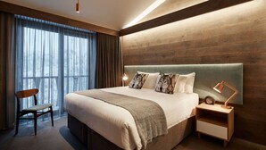 A modern hotel room with a large bed, a wooden headboard, a nightstand with a lamp, and a chair. - Astra Falls Creek (Falls Creek)