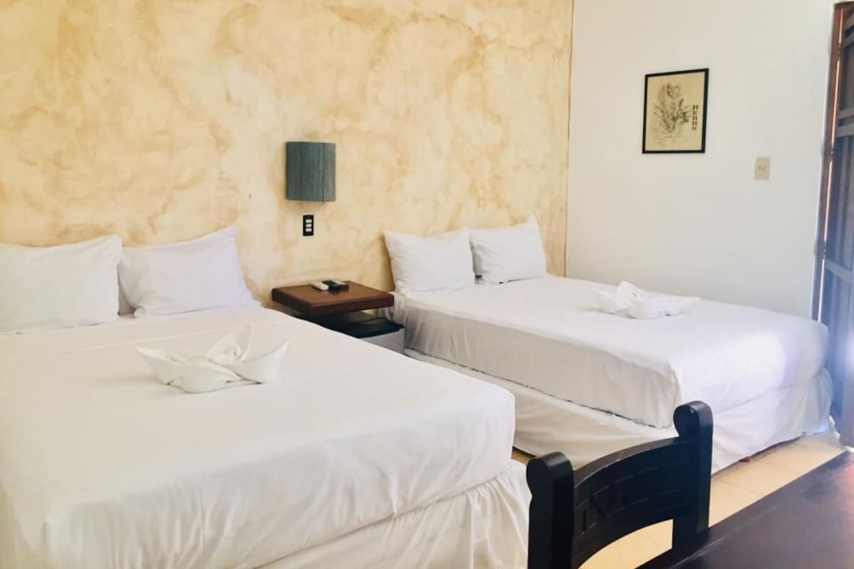 Ein Hotelzimmer mit zwei Einzelbetten, einem Nachttisch, einer Wandlampe und einem gerahmten Bild.