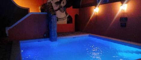 A pool with blue lighting, a mural on the wall, and wall-mounted lights.