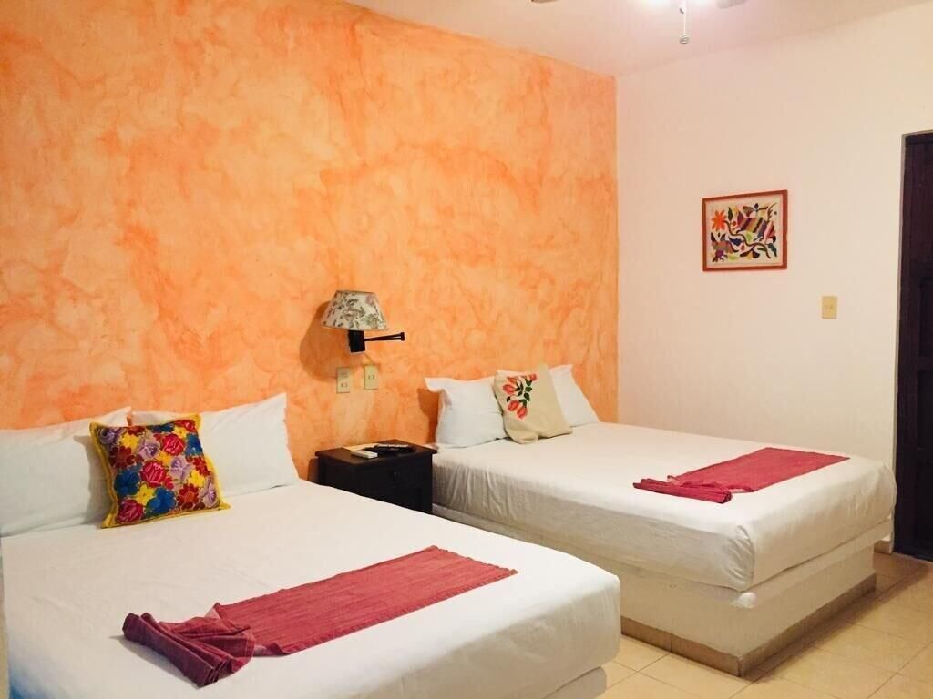 Una habitación de hotel con dos camas, una mesita de noche, una lámpara y un cuadro en la pared.