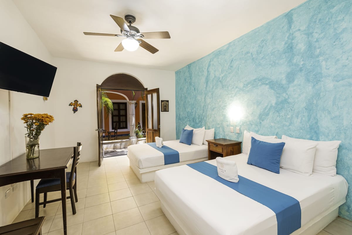 A hotel room with two beds, a desk, and a TV.