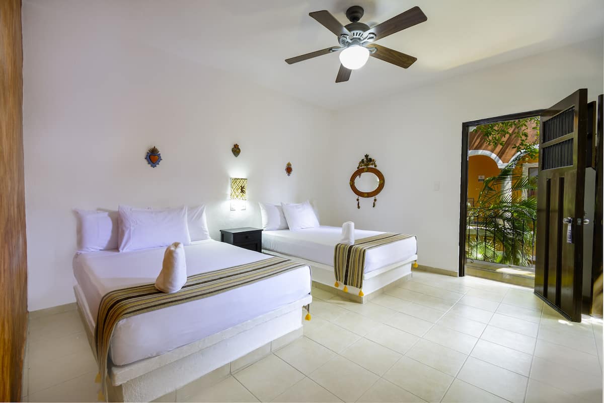 A hotel room with two beds, a ceiling fan, and a view of a garden through an open door.