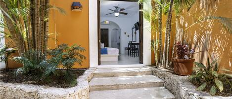 A hotel entrance with a stone staircase leading to a room with a bed, a desk, and a ceiling fan.