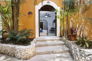 A hotel entrance with a stone staircase leading to a room with a bed, a desk, and a ceiling fan. - Hotel Casa De Las Flores (Playa del Carmen)