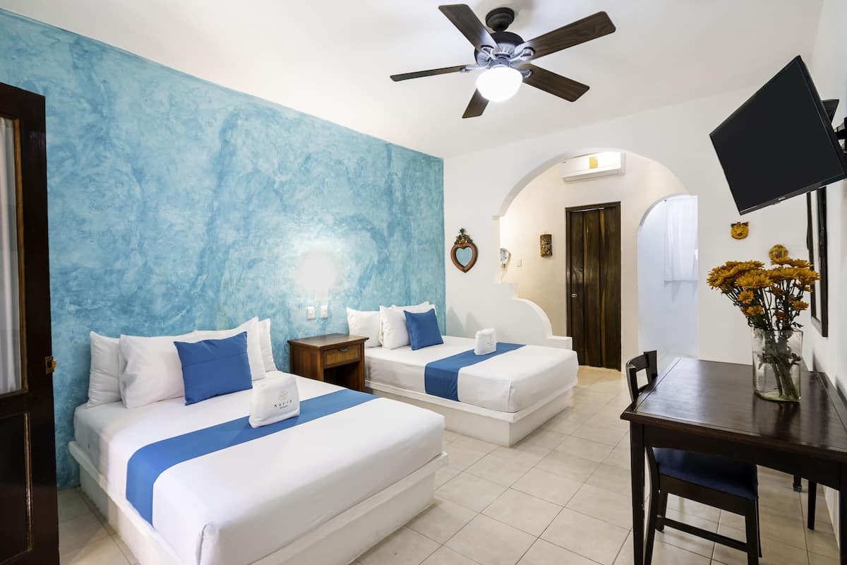 A hotel room with two beds, a ceiling fan, a TV, and a dining table.