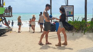 Cena de praia com pessoas caminhando e uma torre de salva-vidas.