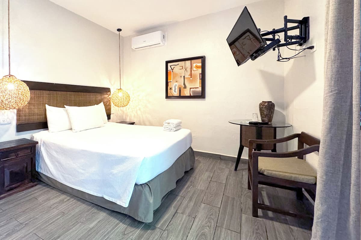 A hotel room with a large bed, bedside tables, a desk, a chair, a TV mounted on the wall, and a framed picture.