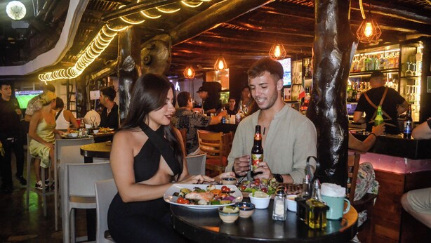 Restaurante com mesas, cadeiras e um espaço de bar com garrafas e copos.