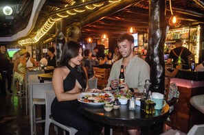 Un restaurante con mesas, sillas y una zona de bar con botellas y vasos.