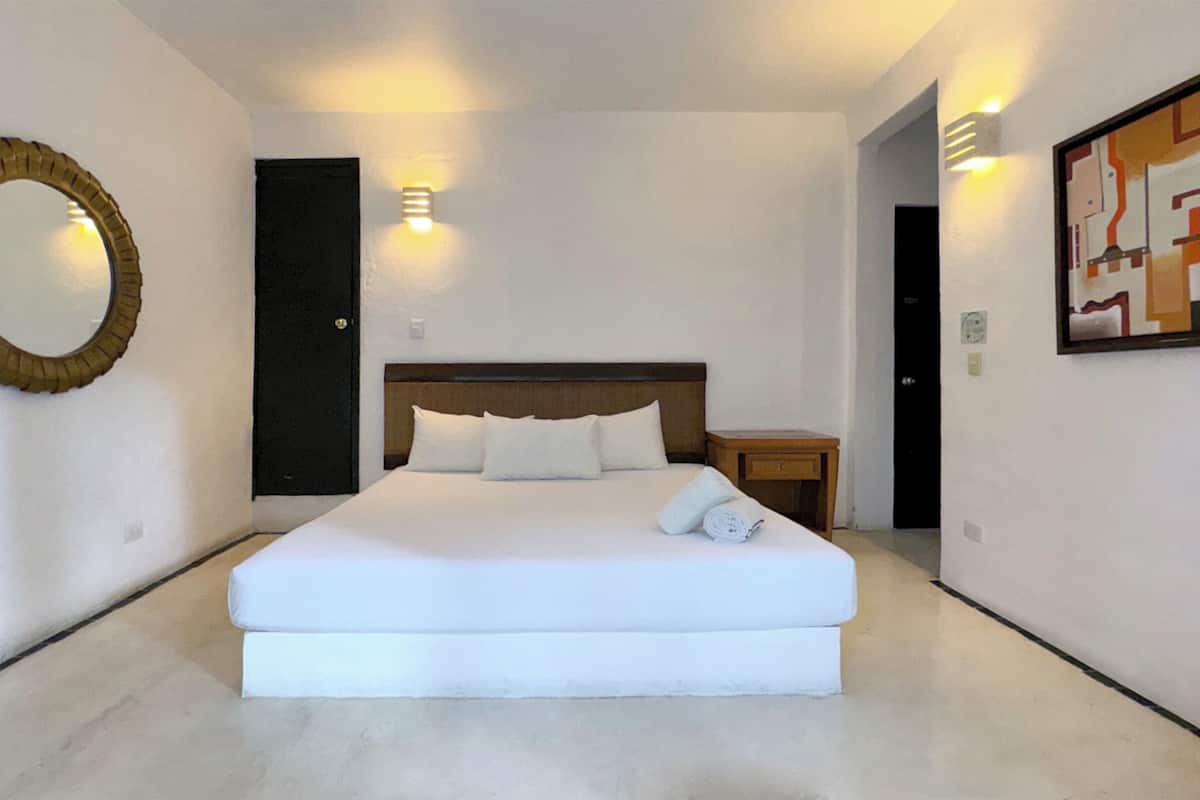 A modern hotel room with a large bed, a round mirror, a nightstand, and a wall-mounted light fixture.