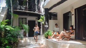Um pátio com piscina, plantas em vasos e área de estar com uma pessoa sentada em uma cadeira.