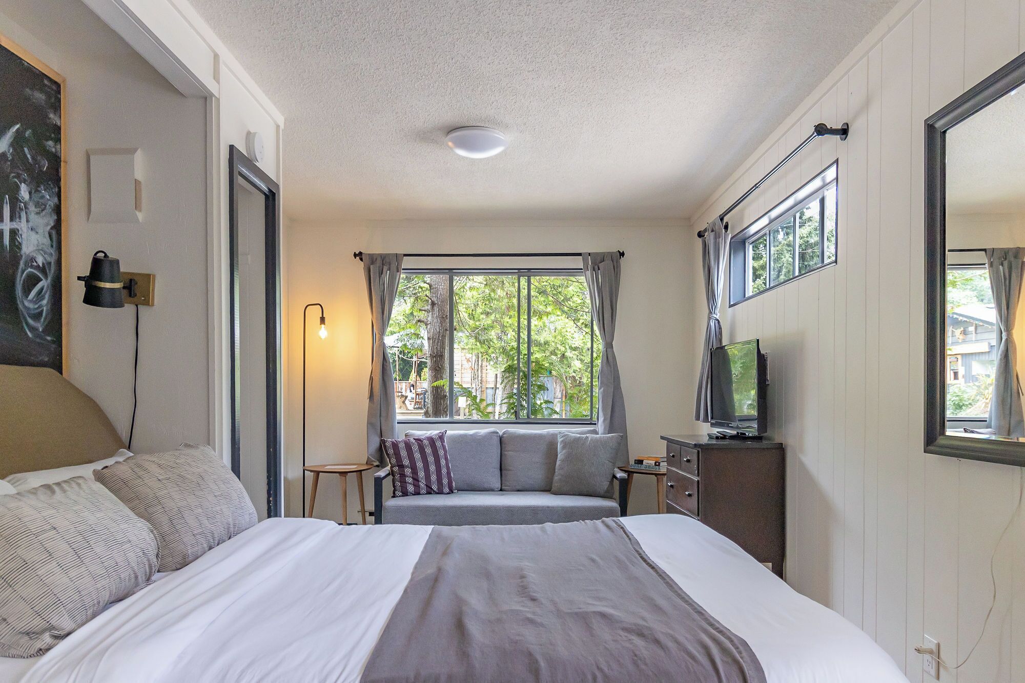 Ein Schlafzimmer mit einem Bett, einem Fernseher, einem Fenster mit Vorhängen und einer Lampe.