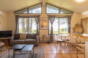 Una sala de estar acogedora con un sofá, una mesa de centro y un televisor. Hay ventanas amplias con cortinas, un comedor con sillas y una mesa.