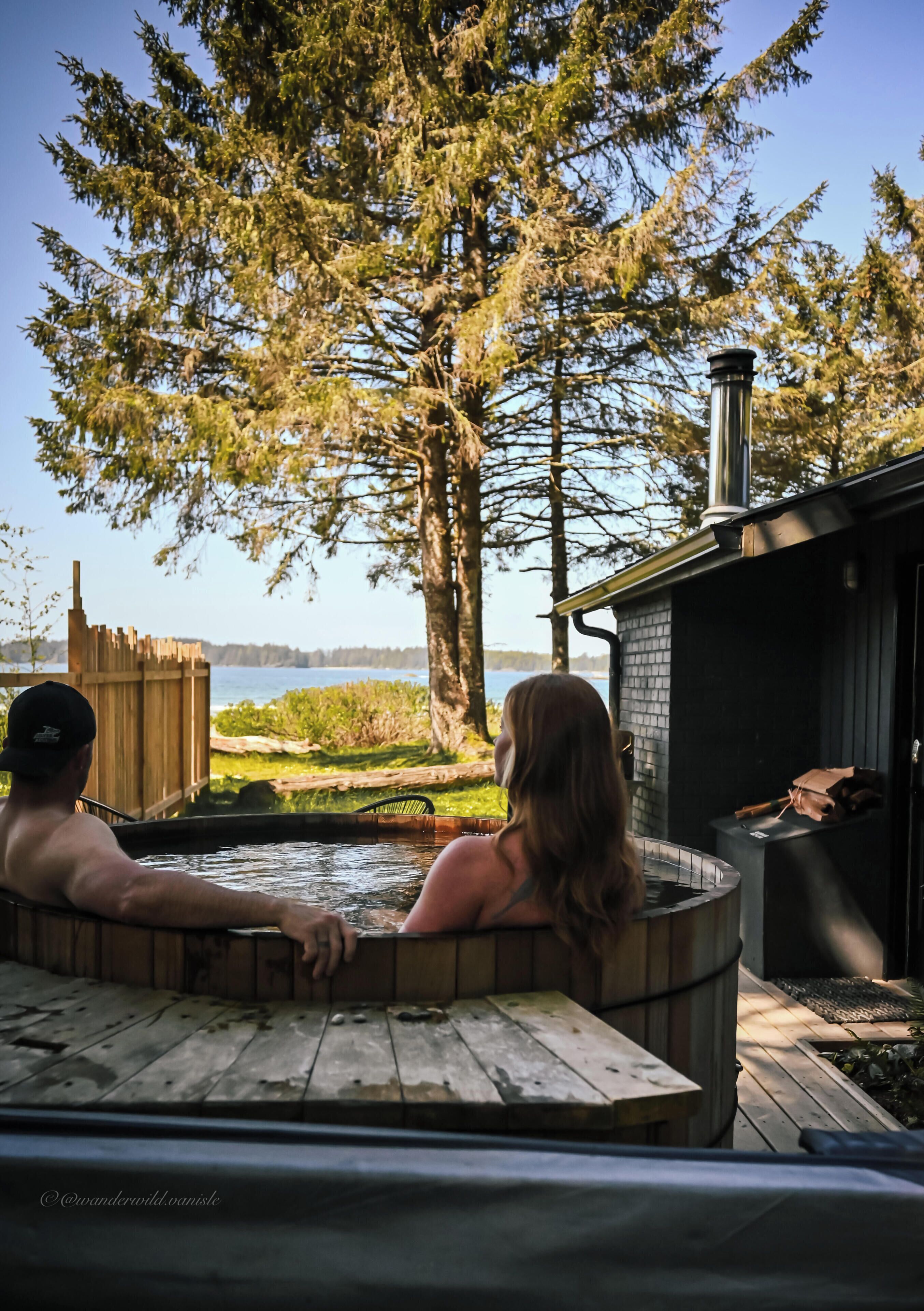 A hot tub with a wooden deck, a brick structure, and a view of a lake and trees.