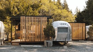 A rustic cabin with a wooden deck and a small porch, surrounded by trees. - Mackenzie Beach Resort (Tofino)