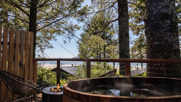 A wooden deck with a hot tub, a chair, and a view of the beach and ocean. - Mackenzie Beach Resort (Tofino)