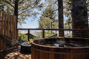 Una terraza de madera con un jacuzzi, una silla y vistas a la playa y al océano.