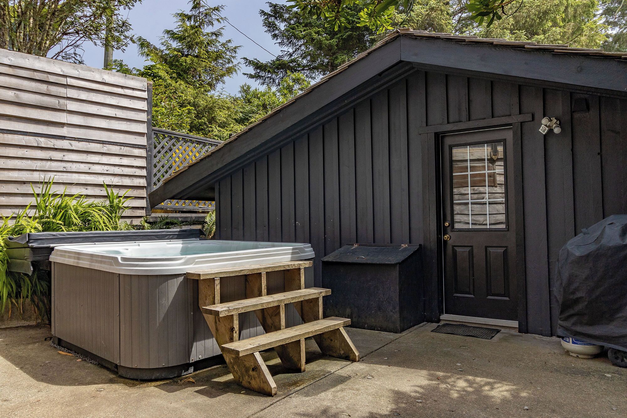 Un bain à remous et des marches en bois dans un jardin, avec un abri sombre et une clôture en bois.