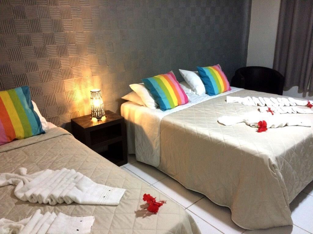 A hotel room with two beds, each with a different pillow design, a nightstand with a lamp, and a chair.