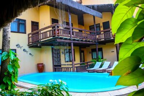 A pool area with a wooden deck, lounge chairs, and a thatched roof structure. - Pousada Capitães de Areia (Ipojuca)