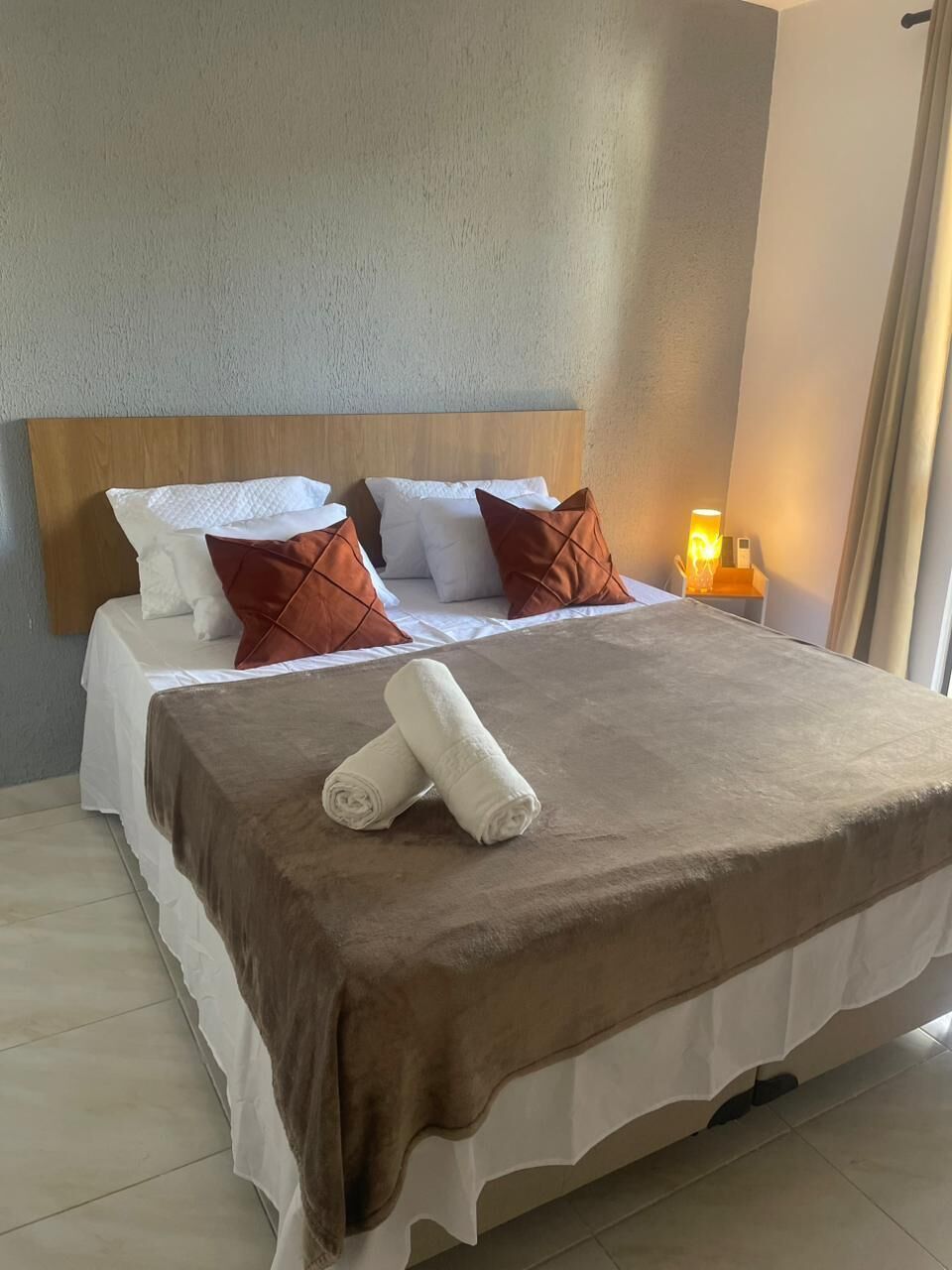 A neatly made bed with a brown bedspread, white linens, and two decorative pillows.