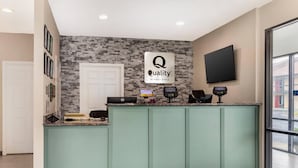 A reception area with a green counter, a 'Quality by Choice Hotels' sign, a TV, and a digital kiosk. - Quality Inn Madison - Huntsville (Madison)