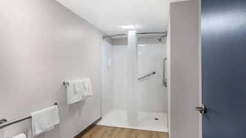 A modern bathroom with a shower, toilet paper, and towels on a rack.