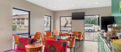 A restaurant with orange chairs, a buffet with food, and large windows.