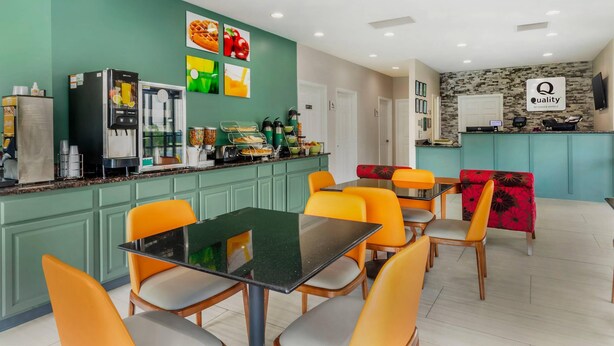 A hotel kitchen with a green wall, a coffee machine, a refrigerator, and a counter with various food items. - Quality Inn Madison - Huntsville (Madison)