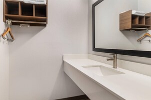 A modern bathroom with a white sink, a mirror, and wooden storage shelves.