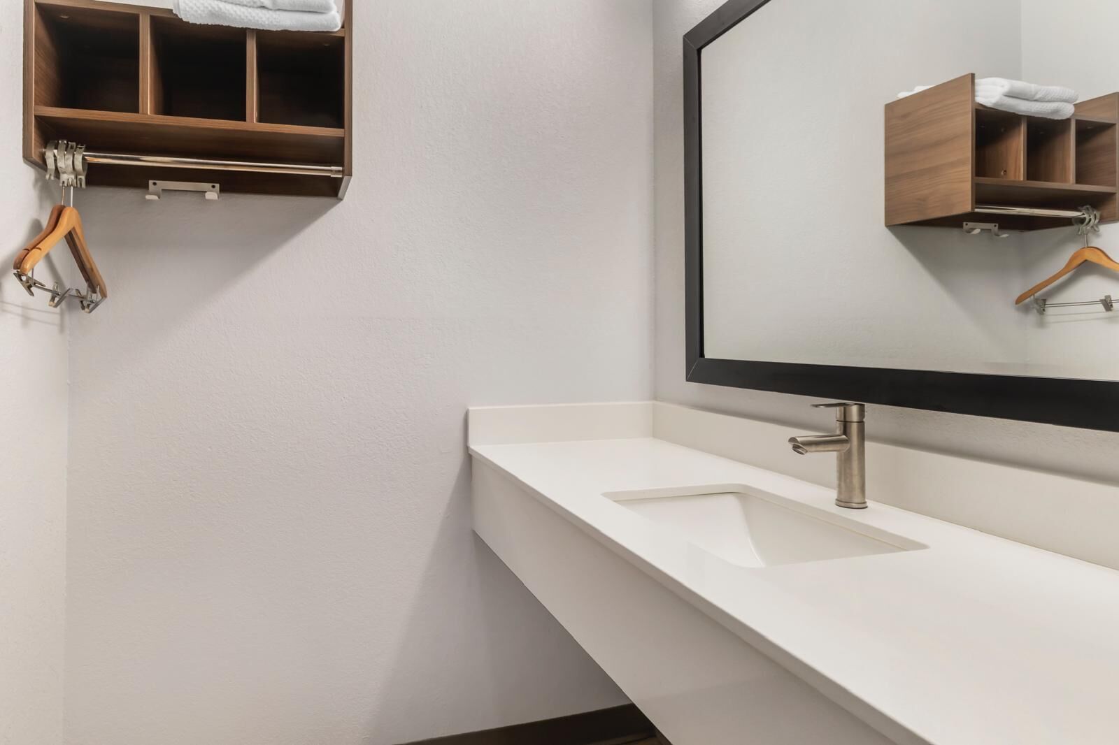 Une salle de bain moderne avec un meuble-lavabo blanc, un grand miroir et un meuble à pharmacie en bois où sont suspendues des serviettes.
