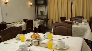 A dining area with tables set for breakfast, including plates, cups, and a basket of pastries. - Hotel América (Mendoza)