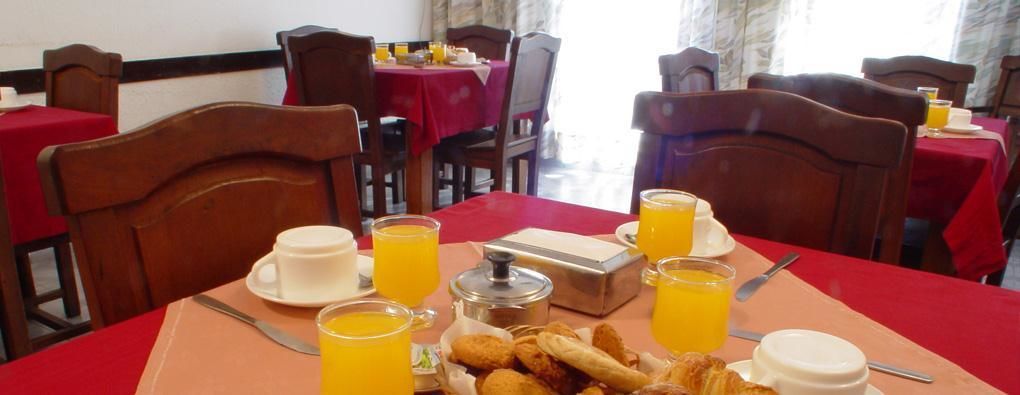 A breakfast setup with orange juice, pastries, and a coffee pot on a red tablecloth.