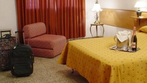 A hotel room with a bed, a chair, a suitcase, and a bottle of wine on the bed. - Hotel América (Mendoza)