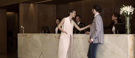 Zona de recepción de un hotel con mostradores de mármol, un mostrador de atención al cliente y un cartel que dice 'DAZZLE HOTEL MEXICO'.