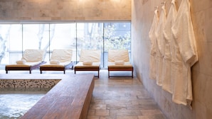 Een wellnessruimte met een houten bank, lounge stoelen, een betegelde vloer en handdoeken aan een muur.