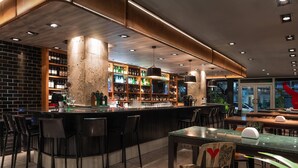Een bar met een gebogen toonbank, zwarte stoelen en planken vol flessen.