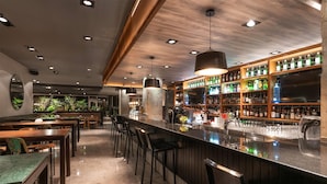 Een bar met houten barstoelen, een lange toonbank en schappen vol flessen.