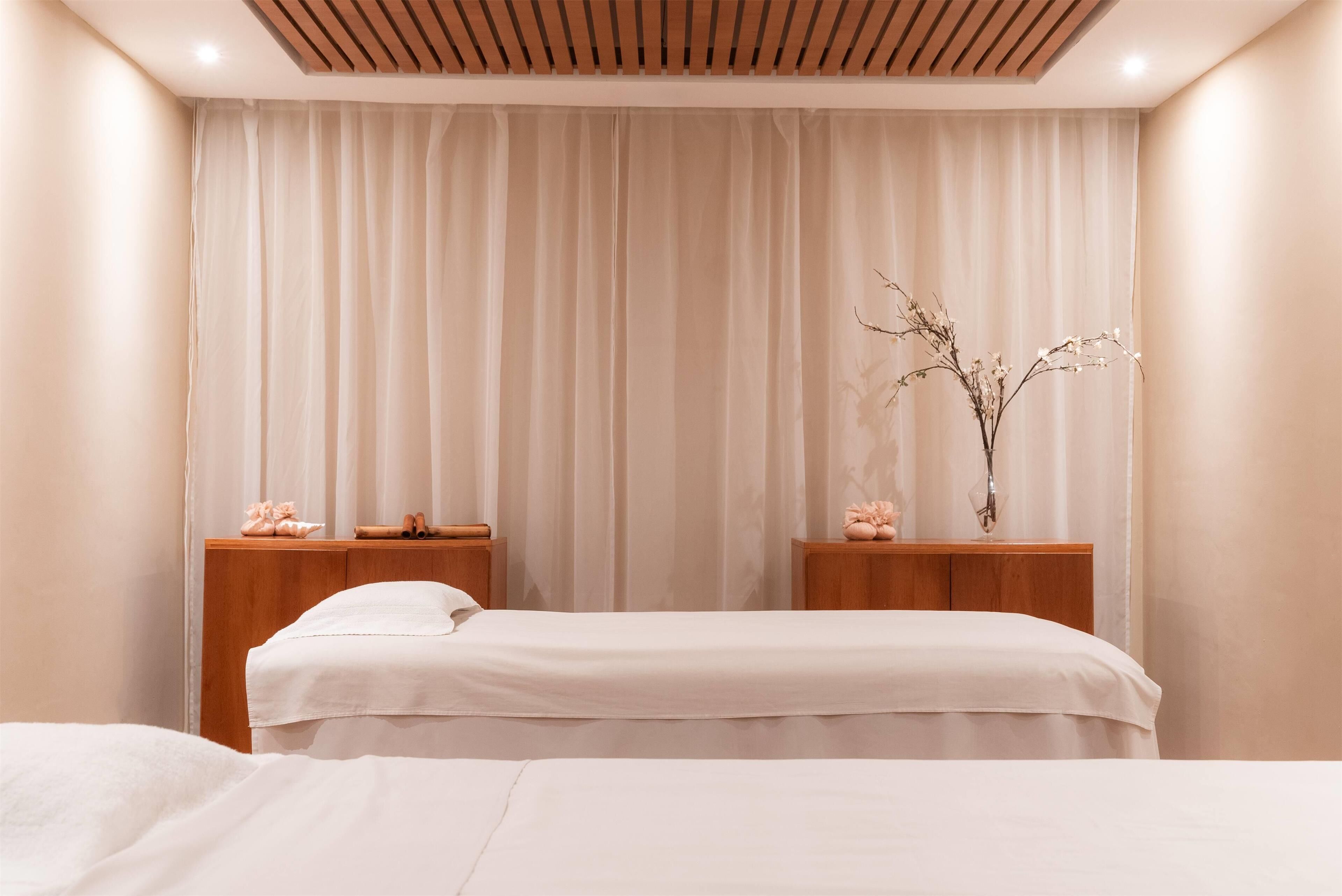 A bedroom with two beds, wooden headboards, and a large window with sheer curtains.