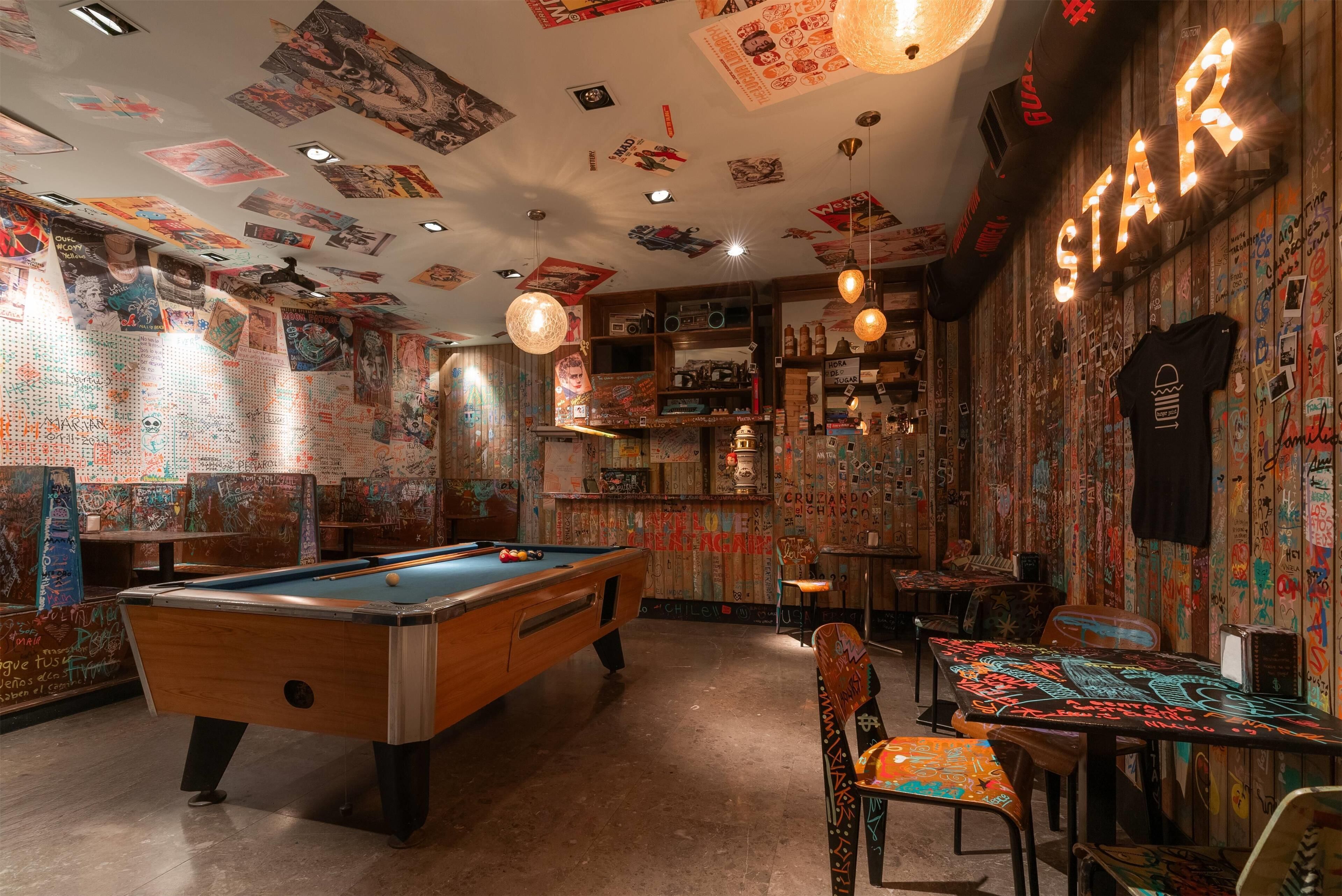 Una mesa de billar en una habitación con paredes cubiertas de grafitis y un letrero de neón que dice 'STAR'.