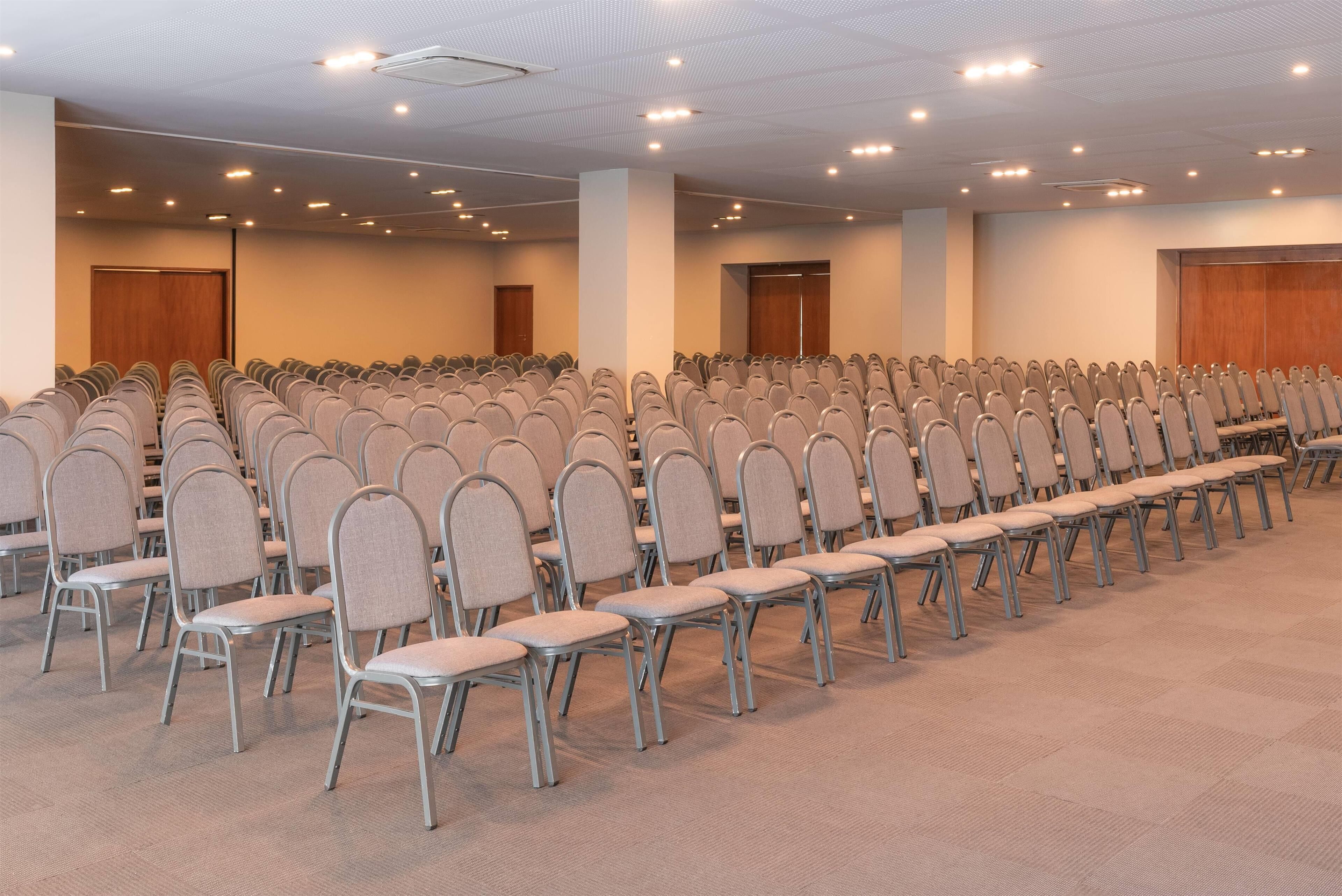 A conference room with rows of chairs, a carpeted floor, and a high ceiling with recessed lighting.