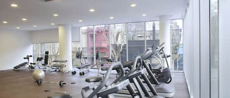 Uma academia com equipamentos de ginástica, grandes janelas e piso de concreto.